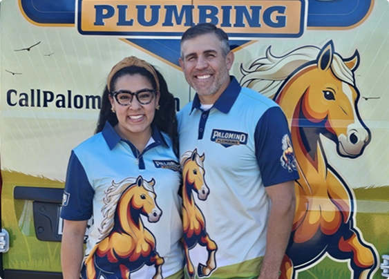 Two people in matching Palomino Plumbing shirts stand and smile in front of a van with horse graphics and company branding.